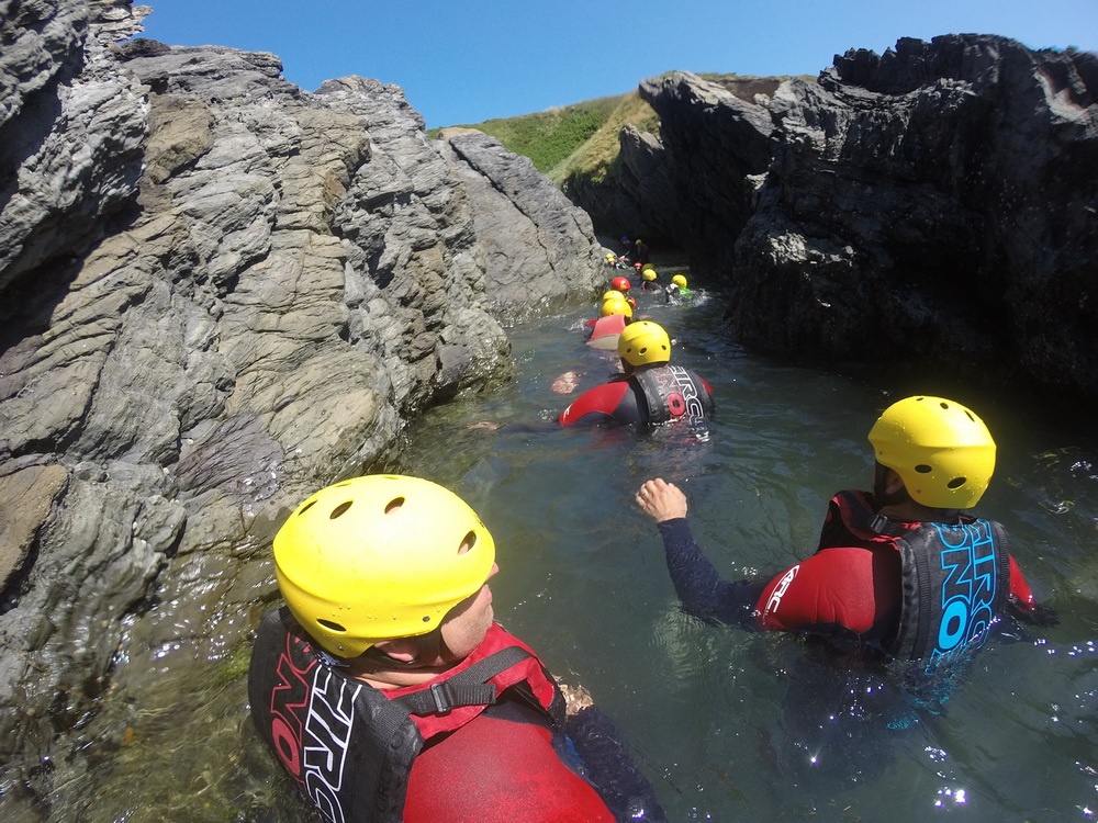 Coasteering participants swimming through sea caves in North Devon